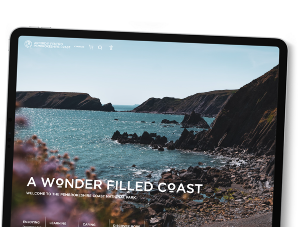 A tablet shows the home page of the Pembrokeshire Coast website