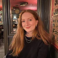 Carrigan, a white woman with long ginger hair smiling and wearing a black top.
                            