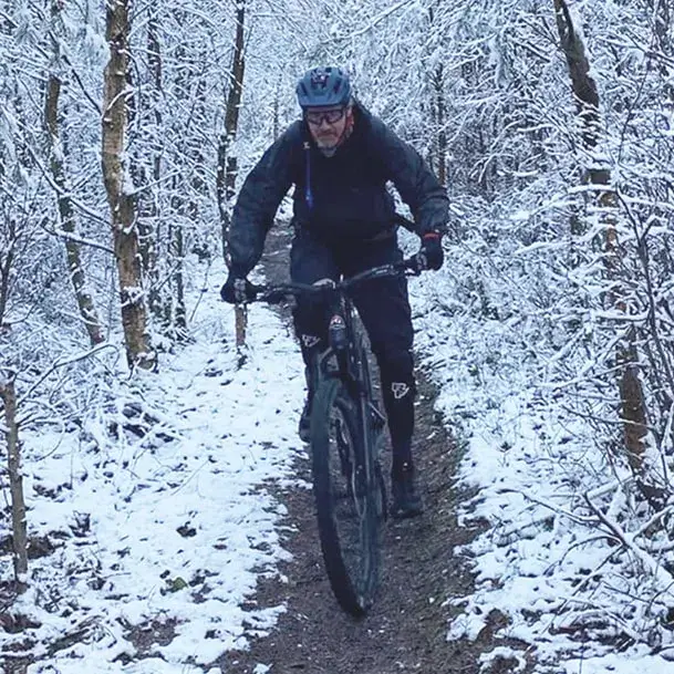 On a snowy woodland path, Joe rides his bike towards the camera