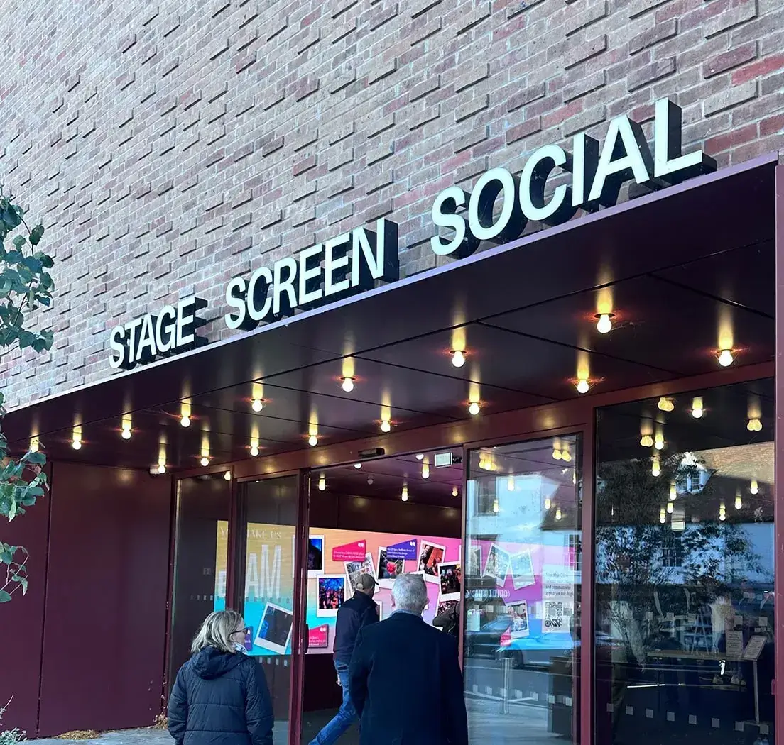 Walking into BEAM Hertford, a large brick building with sliding glass doors, over the door are large letters reading stage. Screen. social. 