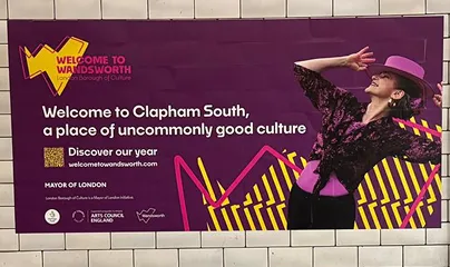 A landscape, purple poster in a tube station with a dancer, a yellow Welcome to Wandsworth logomark and text reading “welcome to Clapham South, a place of uncommonly good culture”