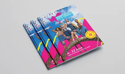 A stack of Wandsworth Arts Fringe brochures, on the cover is an image of a group of happy people over a pink Welcome to Wandsworth logomark